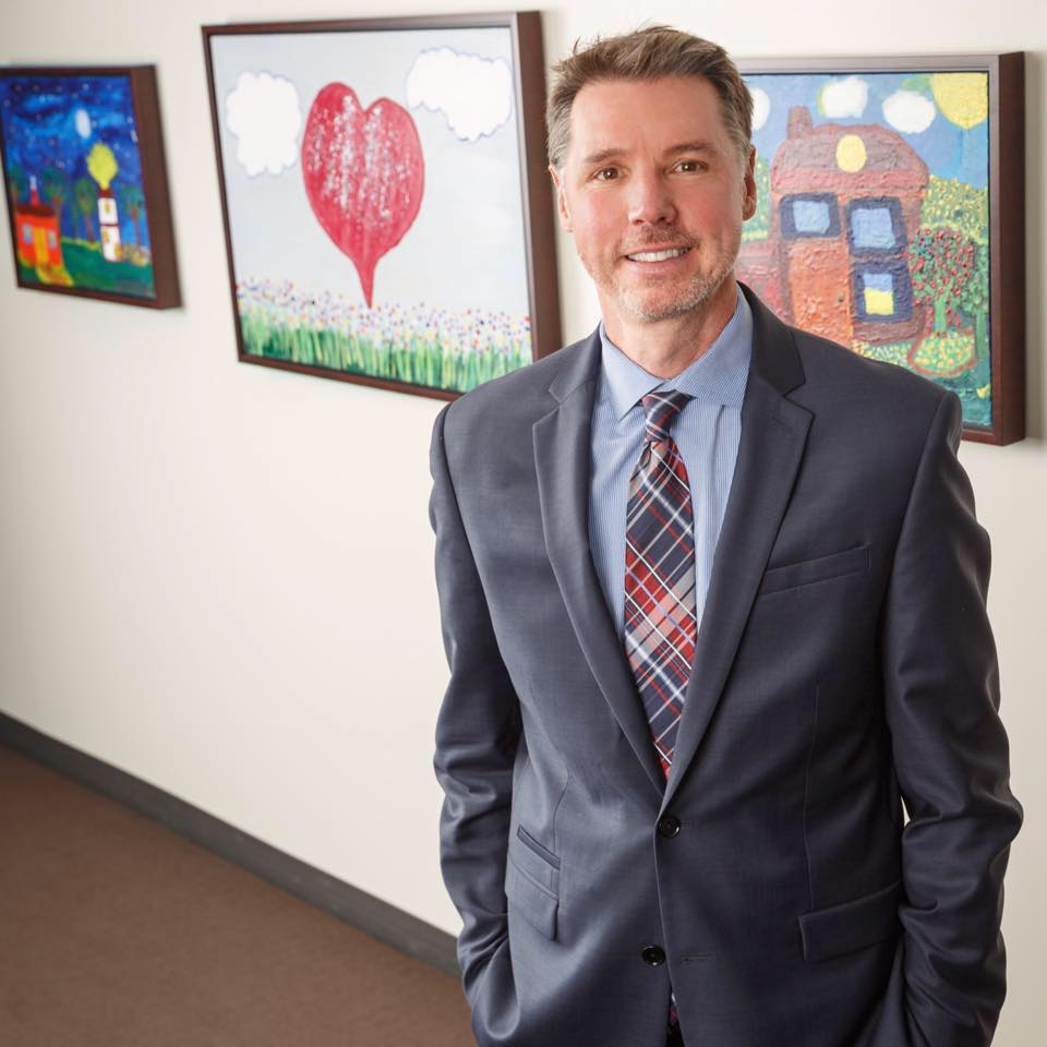 Mark Ishaug standing in front of several pieces of artwork.