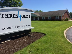 A commercial office sign with Thresholds' logo next to a brown brick building.